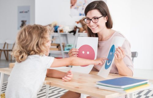 Nauczycielka pokazuje dziecku karty z buźkami emocji